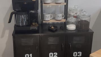Une petite cuisine équipée d’une machine à café, de tasses et de placards de rangement.