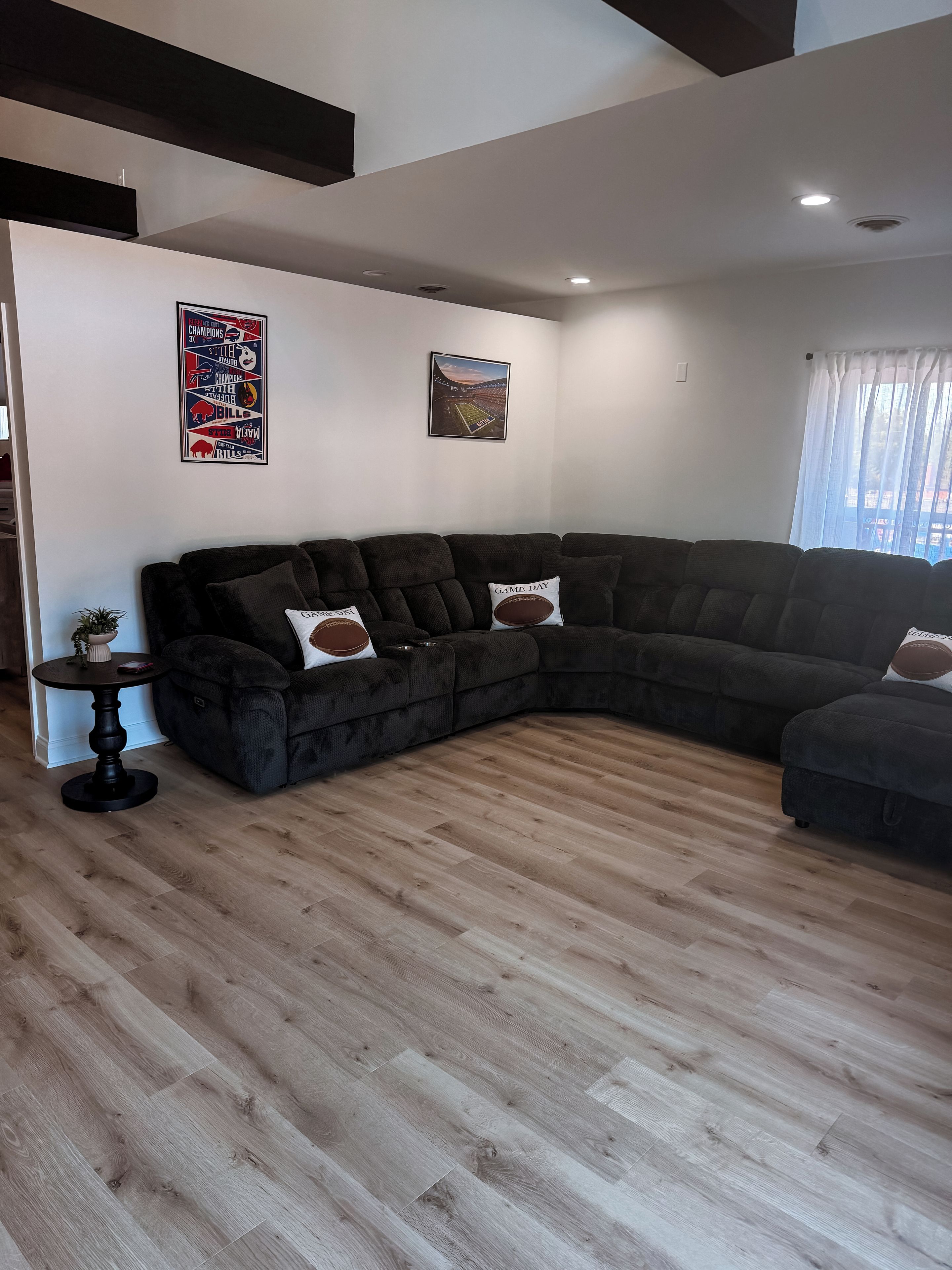 Un salon moderne avec un canapé d’angle, une petite table ronde et un élément de décoration murale sur le thème du sport.
