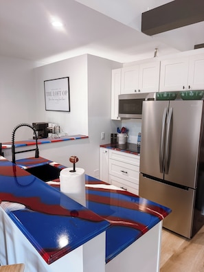 A modern kitchen with white cabinets, a stainless steel refrigerator, and a colorful countertop. - Luxury Loft located in the village of OP, just 7 minutes from Highmark Stadium (Orchard Park)
