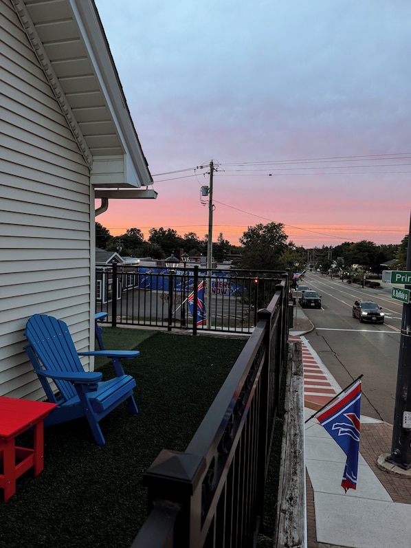 A residential balcony with a blue Adirondack chair, a red chair, and a small red table.