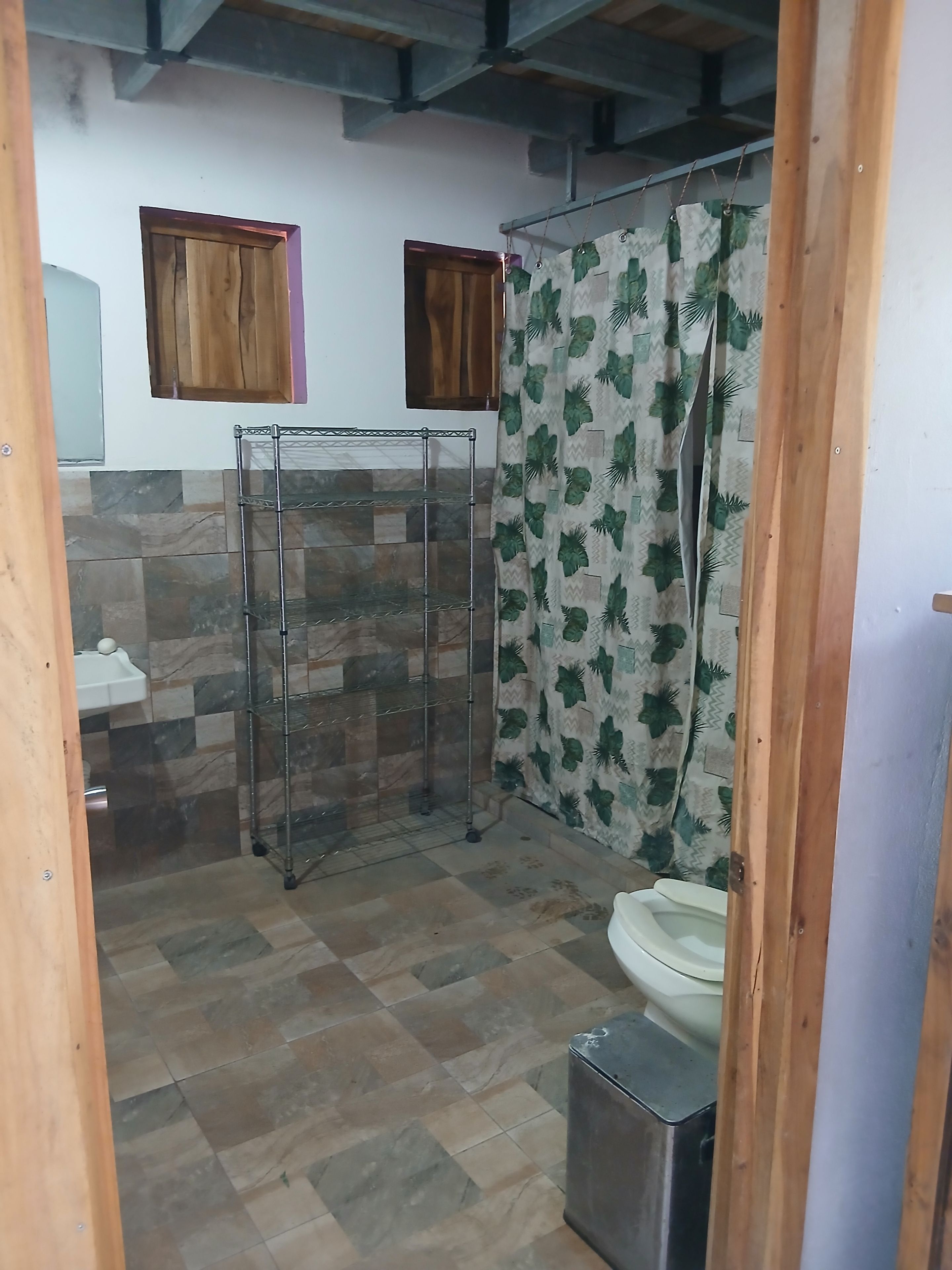 A bathroom with a shower, a toilet, a sink, and a shelf unit.