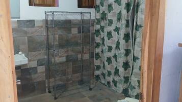 A bathroom with a shower, a toilet, a sink, and a shelf unit.