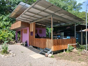 Una construcció rústica de fusta amb una zona exterior coberta, una cuina i un petit jardí.