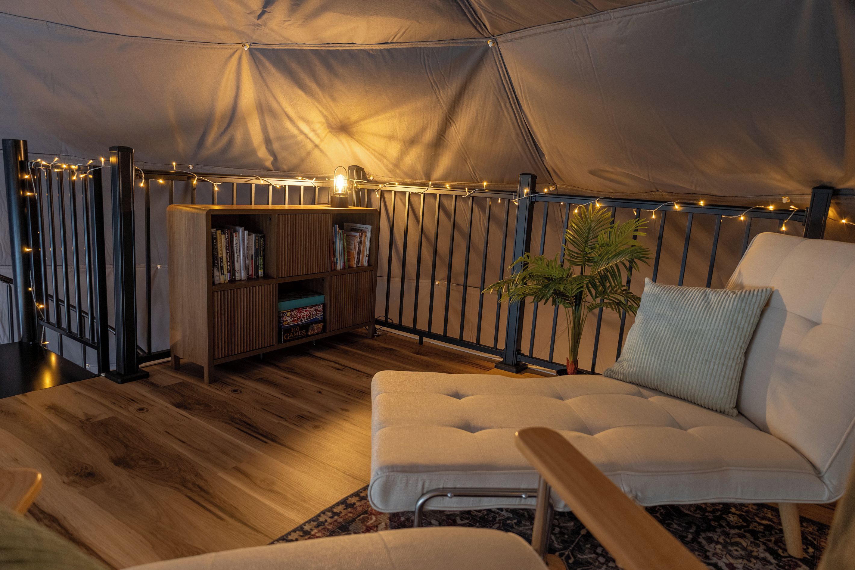 A tent interior with a sofa, bookshelf, and string lights.