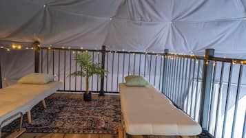 Una habitación con carpa, dos camas, un tapete estampado, una planta en maceta y luces colgantes.