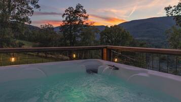 A hot tub with a wooden deck and a view of the sunset and hills.