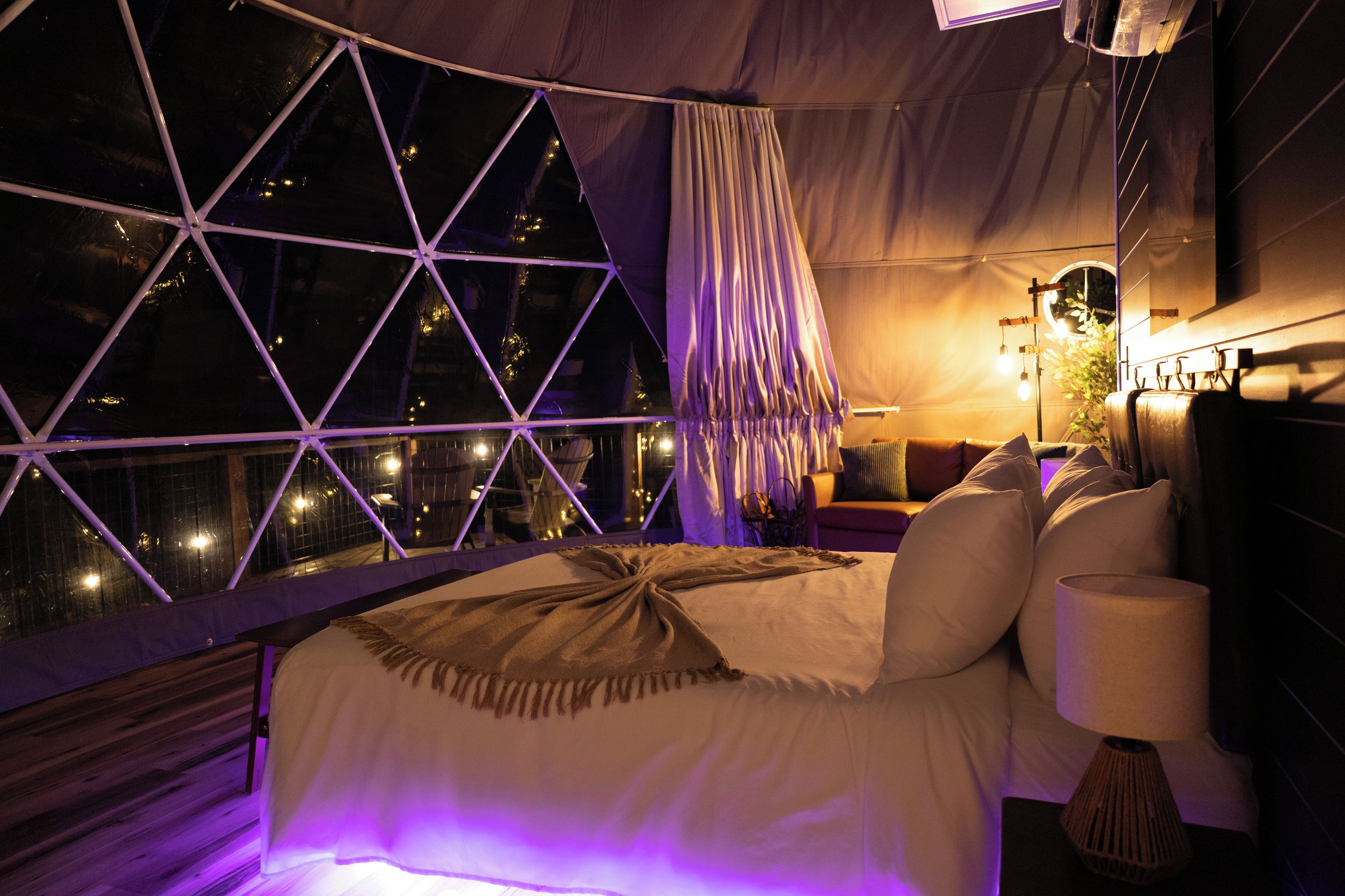 A bedroom with a large window, a bed, and a nightstand with a lamp.