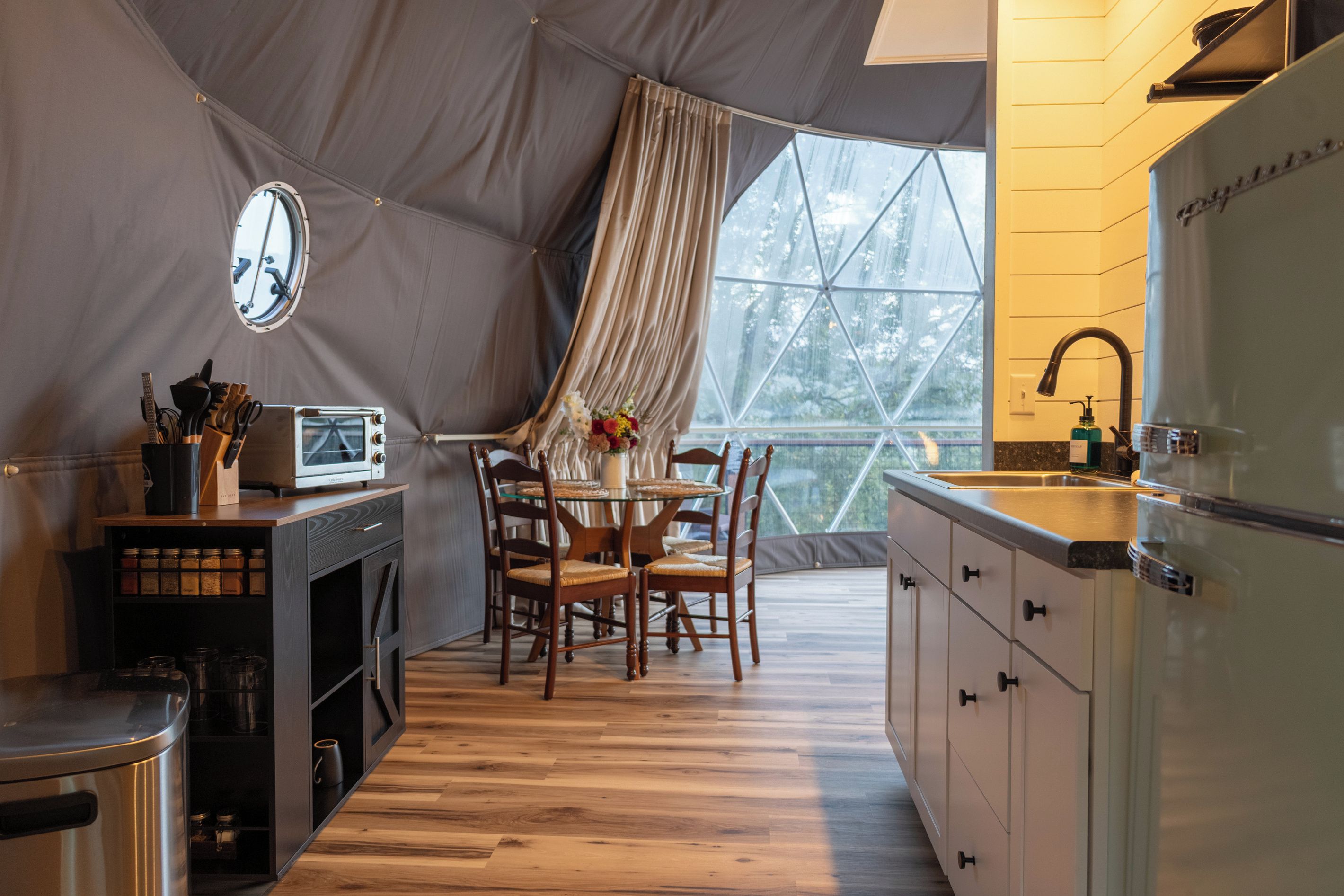 A compact kitchen with a dining area, a large window, and a view of trees.