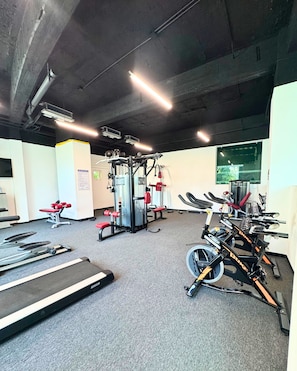 Ein Fitnessstudio mit Laufbändern, Krafttrainingsgeräten und einem an der Wand befestigten Fernseher.