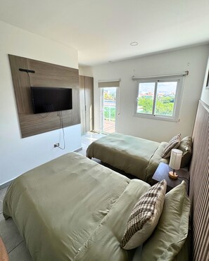 Ein Hotelzimmer mit zwei Betten, einem an der Wand befestigten Fernseher und einem Fenster mit Blick nach draußen.