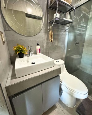 Une salle de bain moderne avec un lavabo blanc, des toilettes, un espace douche et un miroir rond.