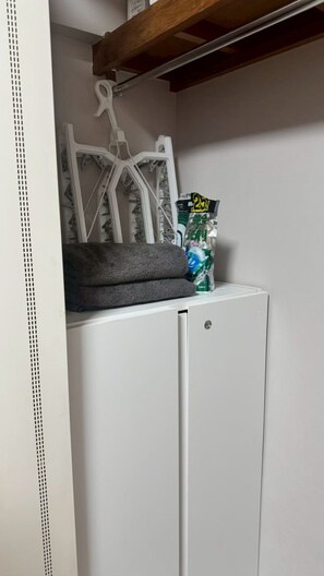 Ein weißer Kleiderschrank mit Kleiderstange, ein Handtuch und eine Tüte Chips.