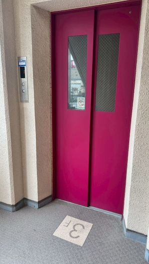 Eine rote Tür mit einem Sicherheitstastaturfeld und einem Schild mit Hinweis auf berührungslose Bedienung.