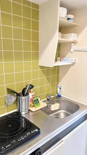 Eine Küche mit einem Edelstahlspülbecken, einer schwarzen Induktionskochplatte und einer grün gefliesten Spritzschutzwand.