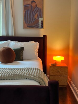 A neatly made bed with pillows, a bedside lamp, and a painting on the wall. - Casa Vida on the Plaza (Kansas City)