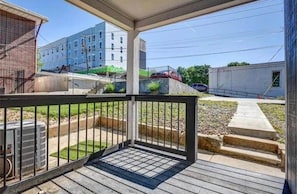 A covered outdoor area with a wooden deck, a metal railing, and a view of a building in the background. - Casa Vida on the Plaza (Kansas City)
