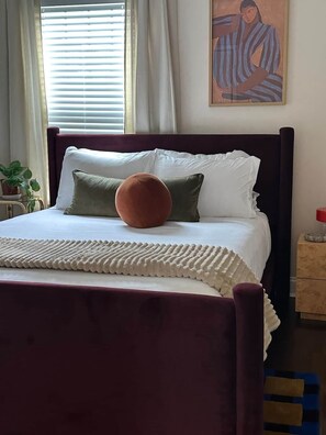 A bed with a dark headboard, white bedding, and a single round orange pillow. - Casa Vida on the Plaza (Kansas City)