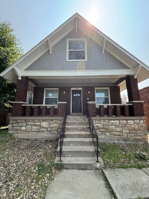 A two-story building with a stone foundation, a front porch with steps, and a black door. - Casa Vida on the Plaza (Kansas City)