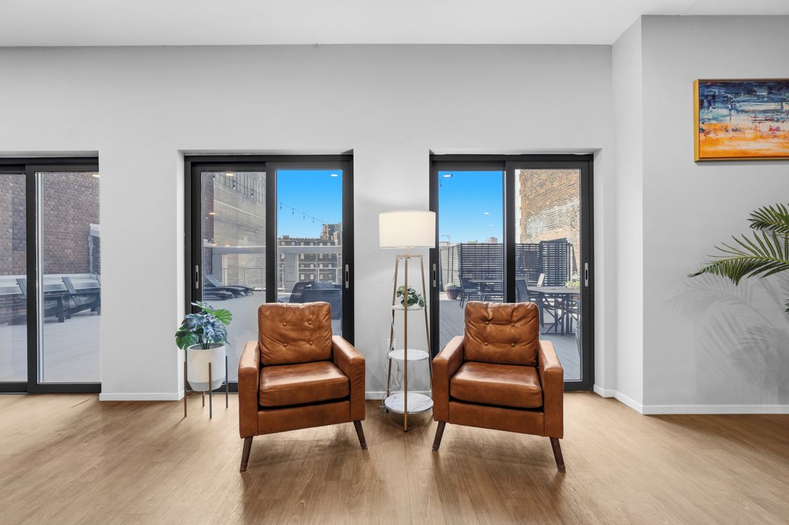 A modern room with two leather armchairs, a floor lamp, and a view of the city through large windows.