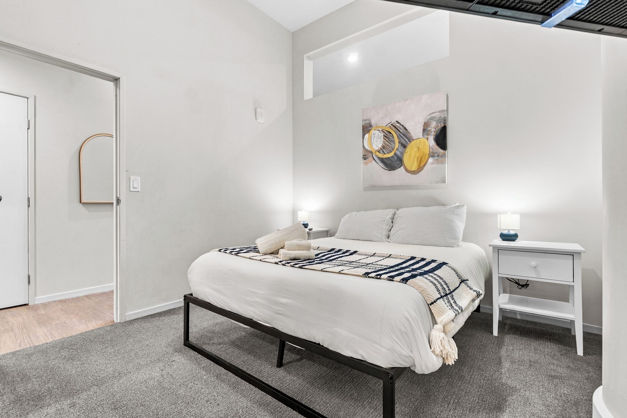 Een moderne slaapkamer met een bed, nachtkastjes en een kunstwerk aan de muur.