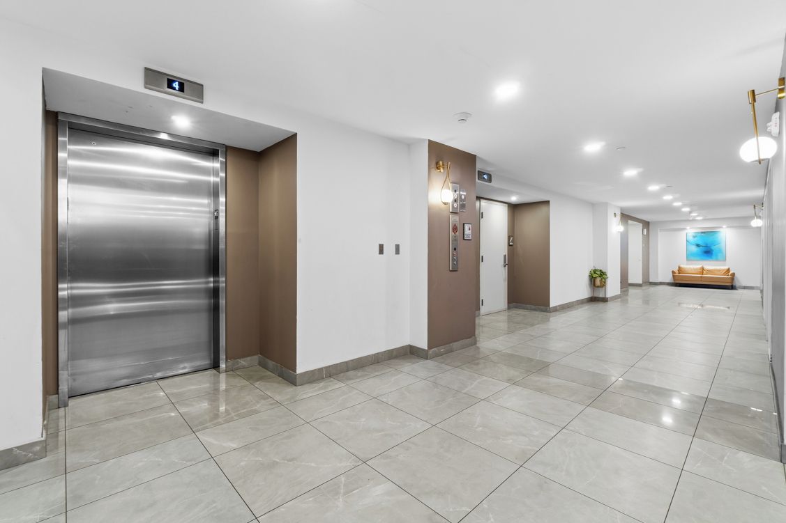 Een moderne hal met een lift, een receptie en een zithoek, met een blauwe muur op de achtergrond.