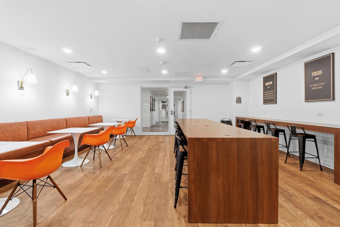 Een modern interieur met een lange houten toonbank, oranje stoelen en witte tafels.