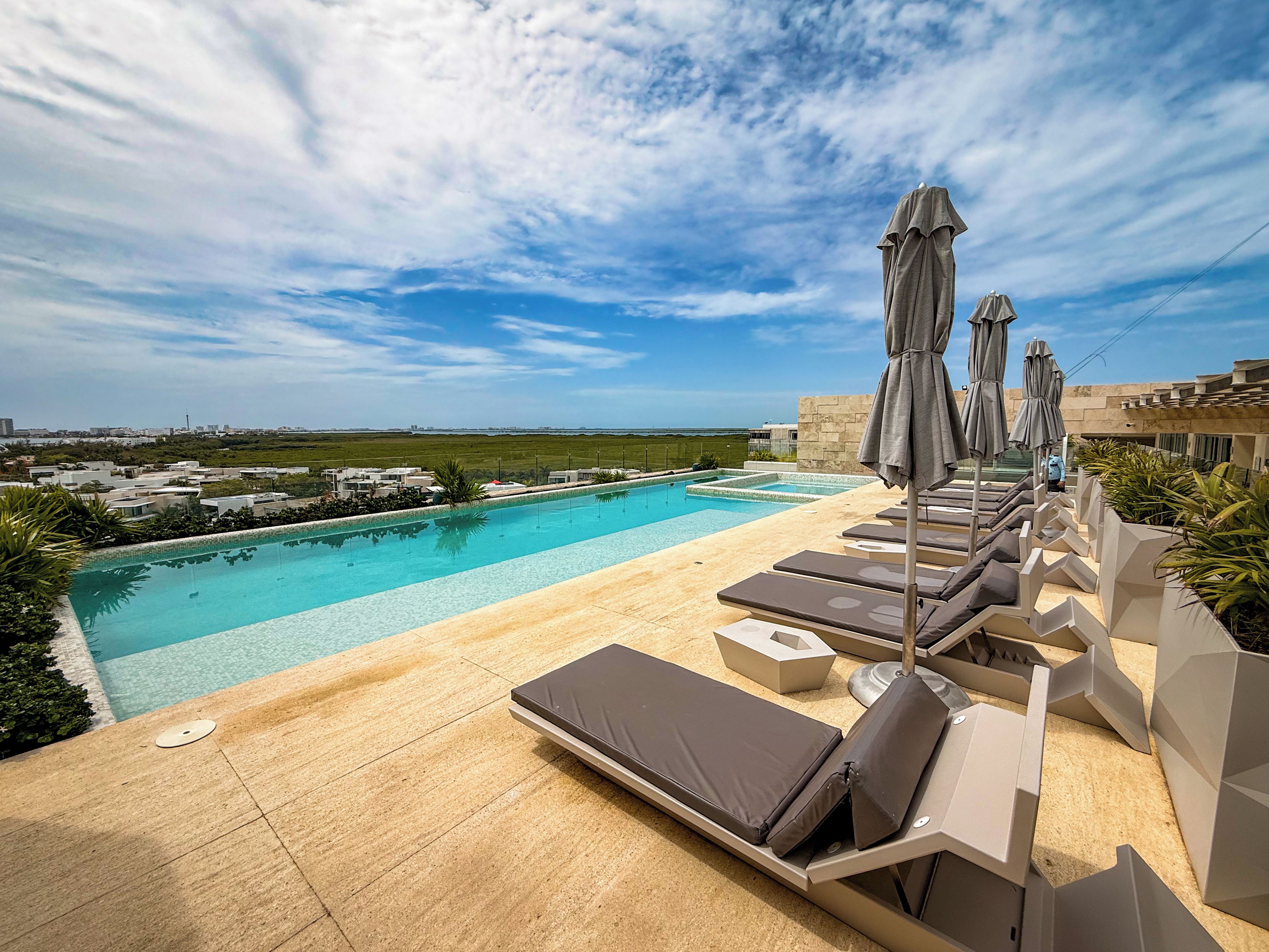 A rooftop pool area with lounge chairs and umbrellas, overlooking a cityscape.