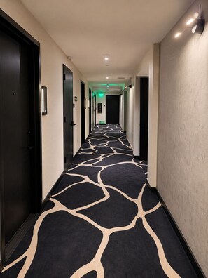 A hotel corridor with a patterned carpet, doors, and a green exit sign. - E11EVEN Executive Penthouse  Luxury Hotel-Style Retreat (Miami)