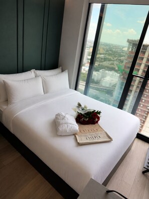 A modern hotel room with a large bed, a view of the city through floor-to-ceiling windows, and a neatly made bed with a towel and a card. - E11EVEN Executive Penthouse  Luxury Hotel-Style Retreat (Miami)