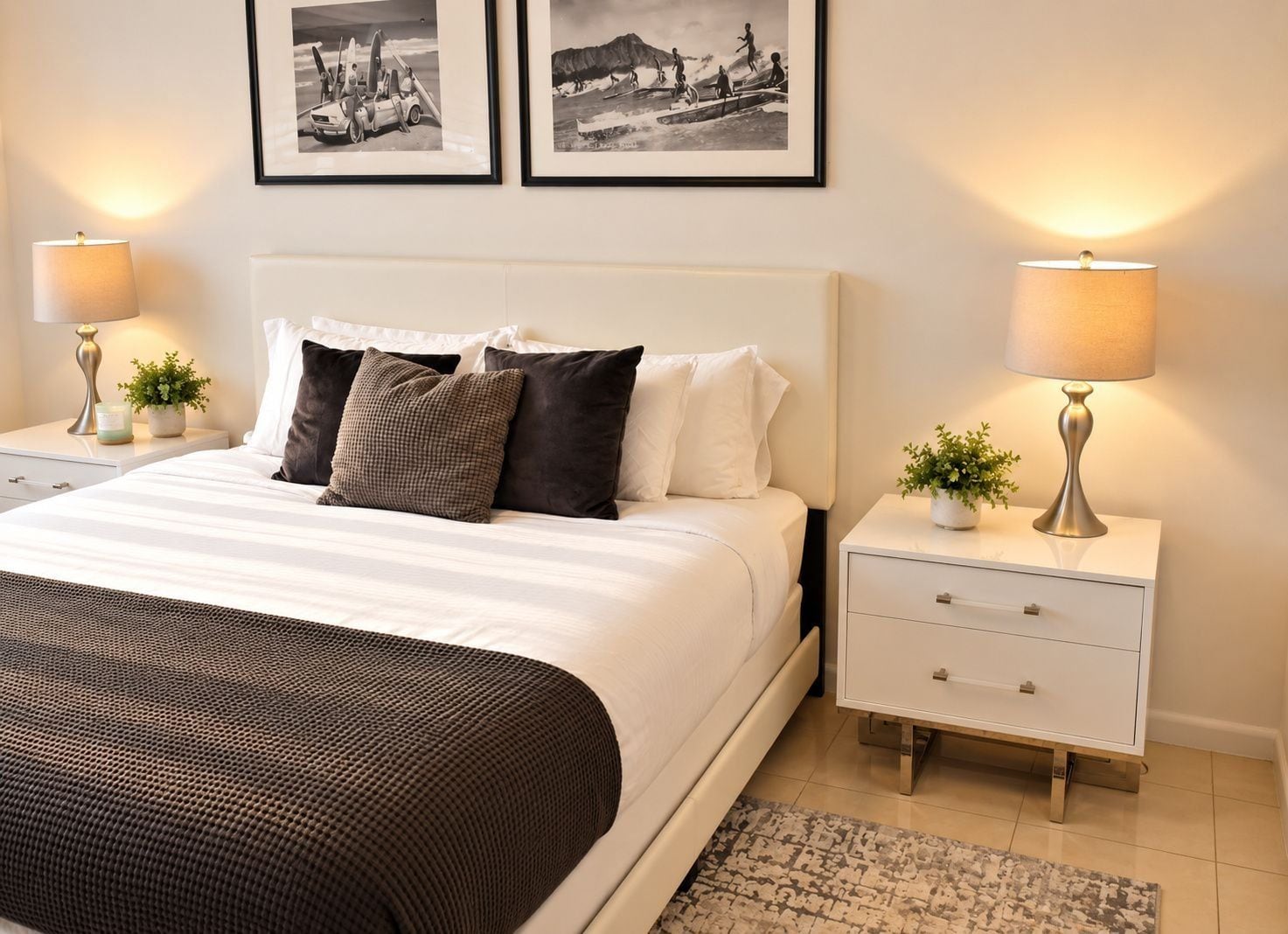 A hotel room with a large bed, two bedside tables with lamps, a small potted plant, and two framed pictures on the wall.