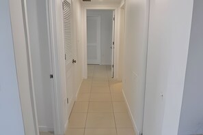 A narrow hallway with white walls and a tiled floor, leading to a door at the end. - Midblock - Pool - Gym - Midtown Miami (Miami)