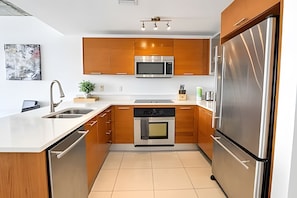A modern kitchen with wooden cabinets, stainless steel appliances, and a white countertop. - Midblock - Pool - Gym - Midtown Miami (Miami)