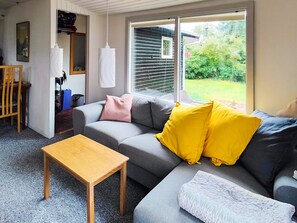 Een moderne woonkamer met een grijze bank, een houten salontafel en uitzicht op een tuin door een schuifdeur.
