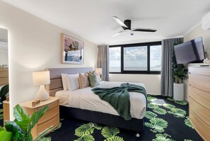 Una camera d'hotel con un letto, un comodino, una televisione, una ventola a soffitto e un'ampia finestra vista mare.