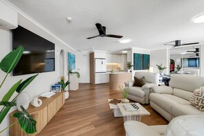 A modern living room with a sofa, coffee table, and a TV mounted on the wall. - Belle Escapes Aquarius' Panoramic Jewel 11th Floor (Cairns City)