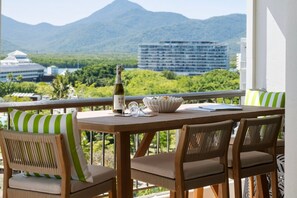 A balcony with a wooden table, wicker chairs, and a bottle of champagne. - Belle Escapes Aquarius' Panoramic Jewel 11th Floor (Cairns City)