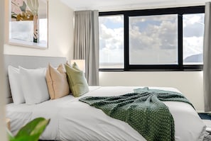 A hotel room with a bed, a window with a view of the sky, and a painting on the wall. - Belle Escapes Aquarius' Panoramic Jewel 11th Floor (Cairns City)