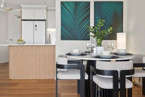A modern dining area with a round table, chairs, and a central island with a bowl of fruit. - Belle Escapes Aquarius' Panoramic Jewel 11th Floor (Cairns City)
