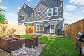 Ein zweistöckiges Haus mit eingezäuntem Garten, Gartenmöbeln und einem Grill.