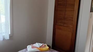 A room with a bed, a wooden door, and a window with sheer curtains.