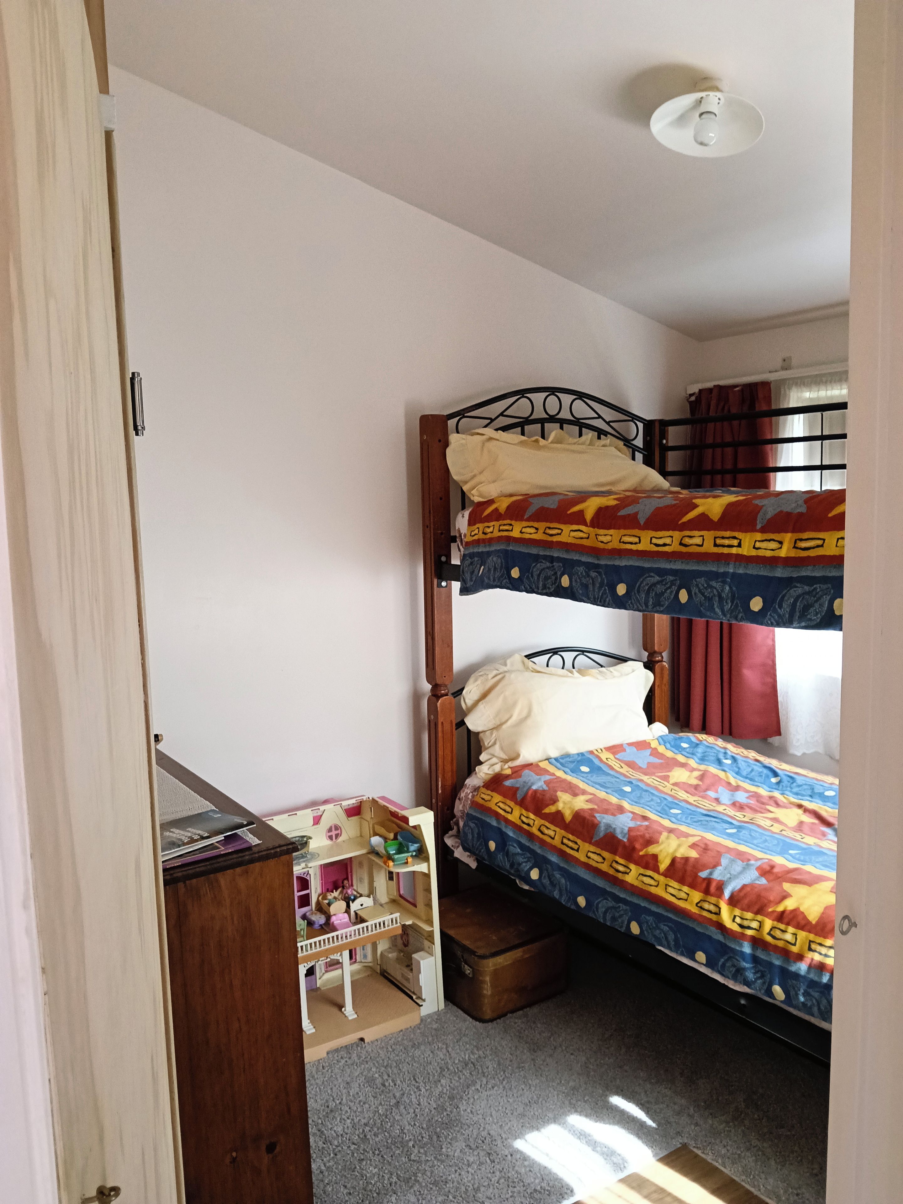 A room with a bunk bed, a small wooden desk, and a toy house.