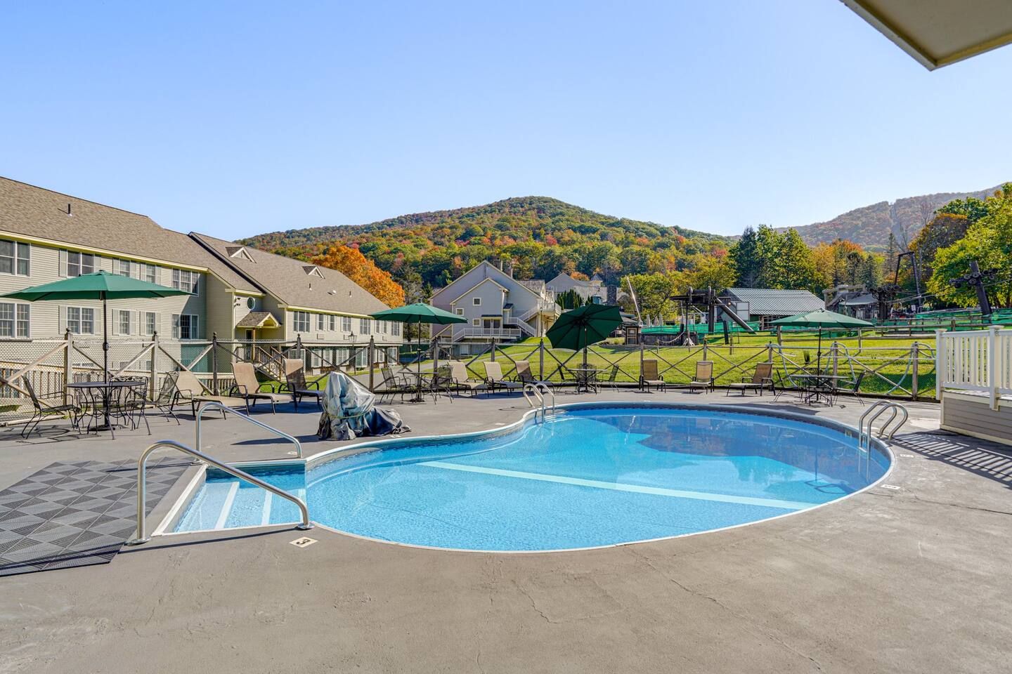 Une piscine entourée de bâtiments et d’un paysage vallonné, avec des chaises longues et des parasols à proximité.