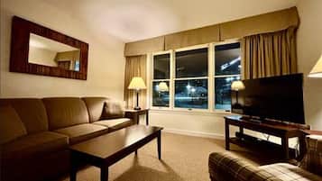 A living room with a sofa, a coffee table, a television, and a window with curtains.