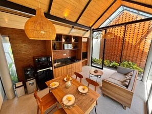 Uma cozinha moderna com armários de madeira, sala de jantar com mesa e cadeiras de madeira, e área de estar com sofá e uma pequena mesa redonda.