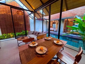 A dining area with a pool view, featuring a table set for four with plates, cutlery, and a centerpiece. - Villa Jia by Kelle, Ubud (Gianyar)