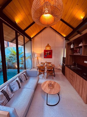 A modern interior with a wooden ceiling, a dining area with a table and chairs, a sofa, and a kitchen area with cabinets and a sink. - Villa Jia by Kelle, Ubud (Gianyar)