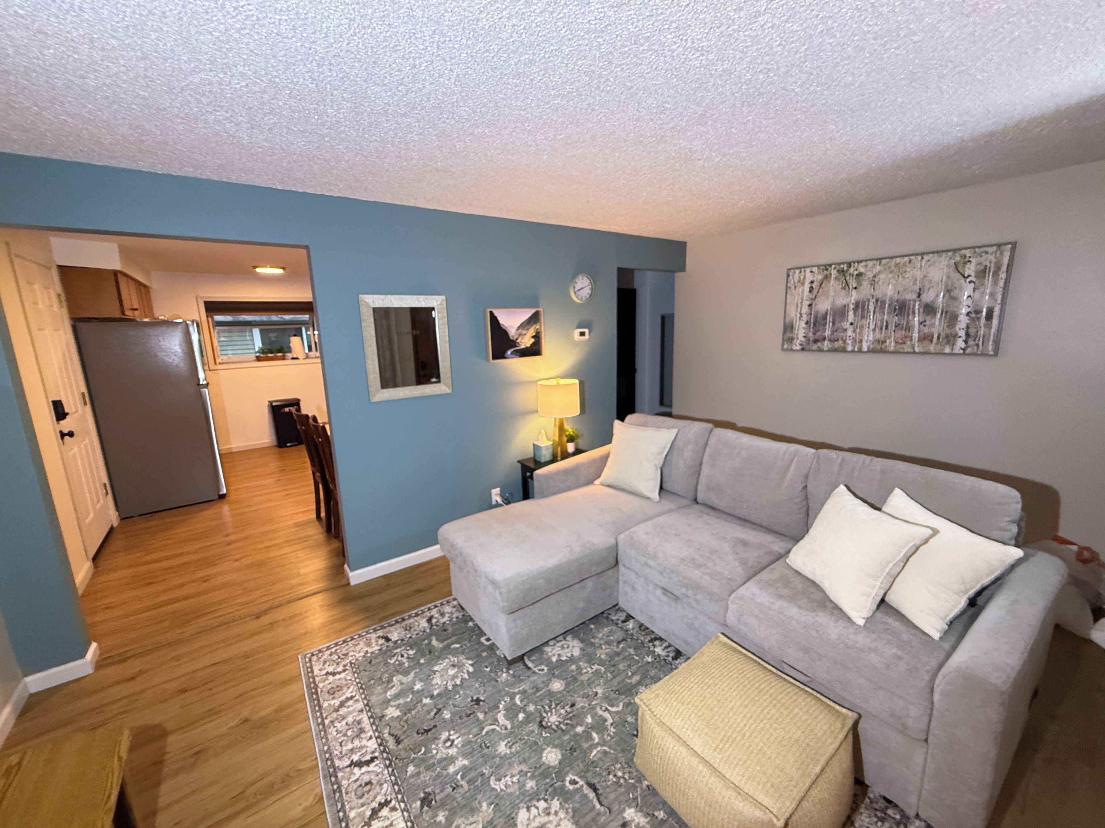 A living room with a grey sectional sofa, a small rug, and a painting on the wall.