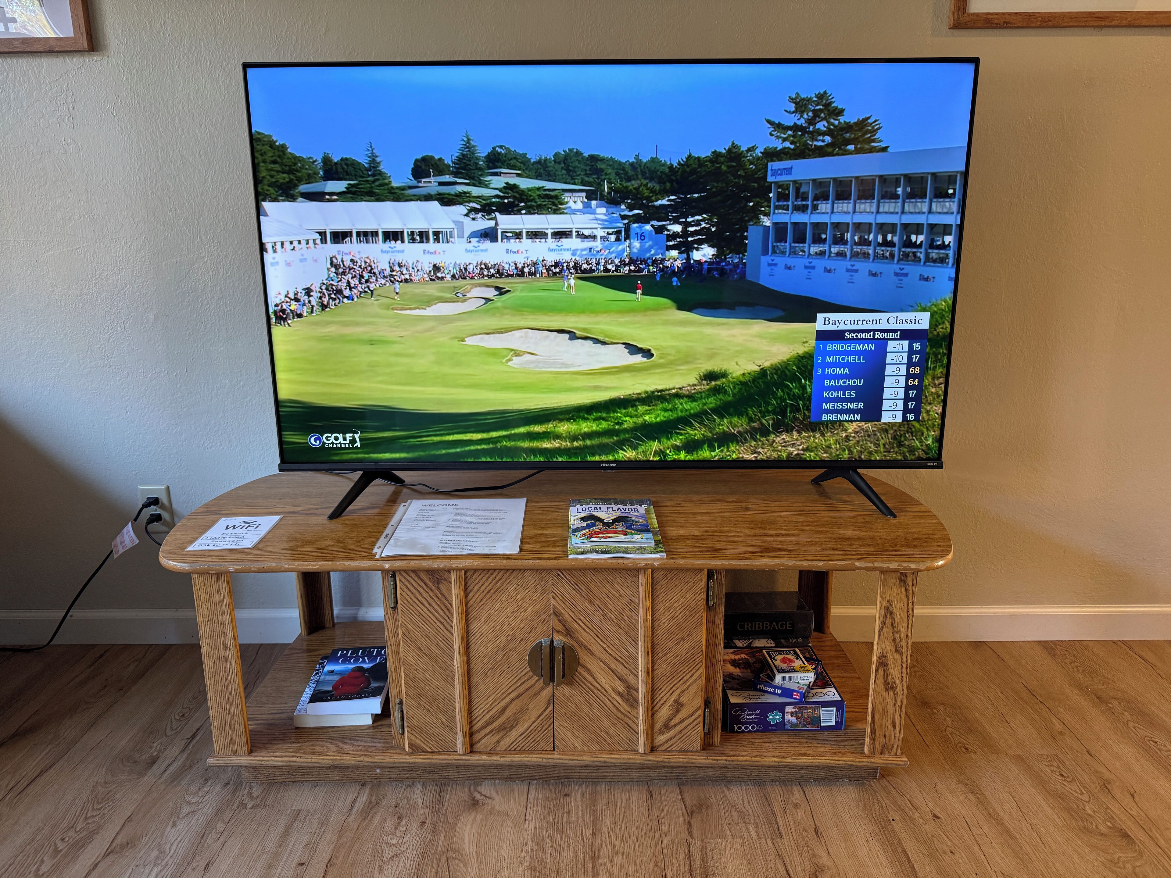 Un téléviseur posé sur un meuble en bois, diffusant une image d’un terrain de golf avec un tableau d’affichage des scores.