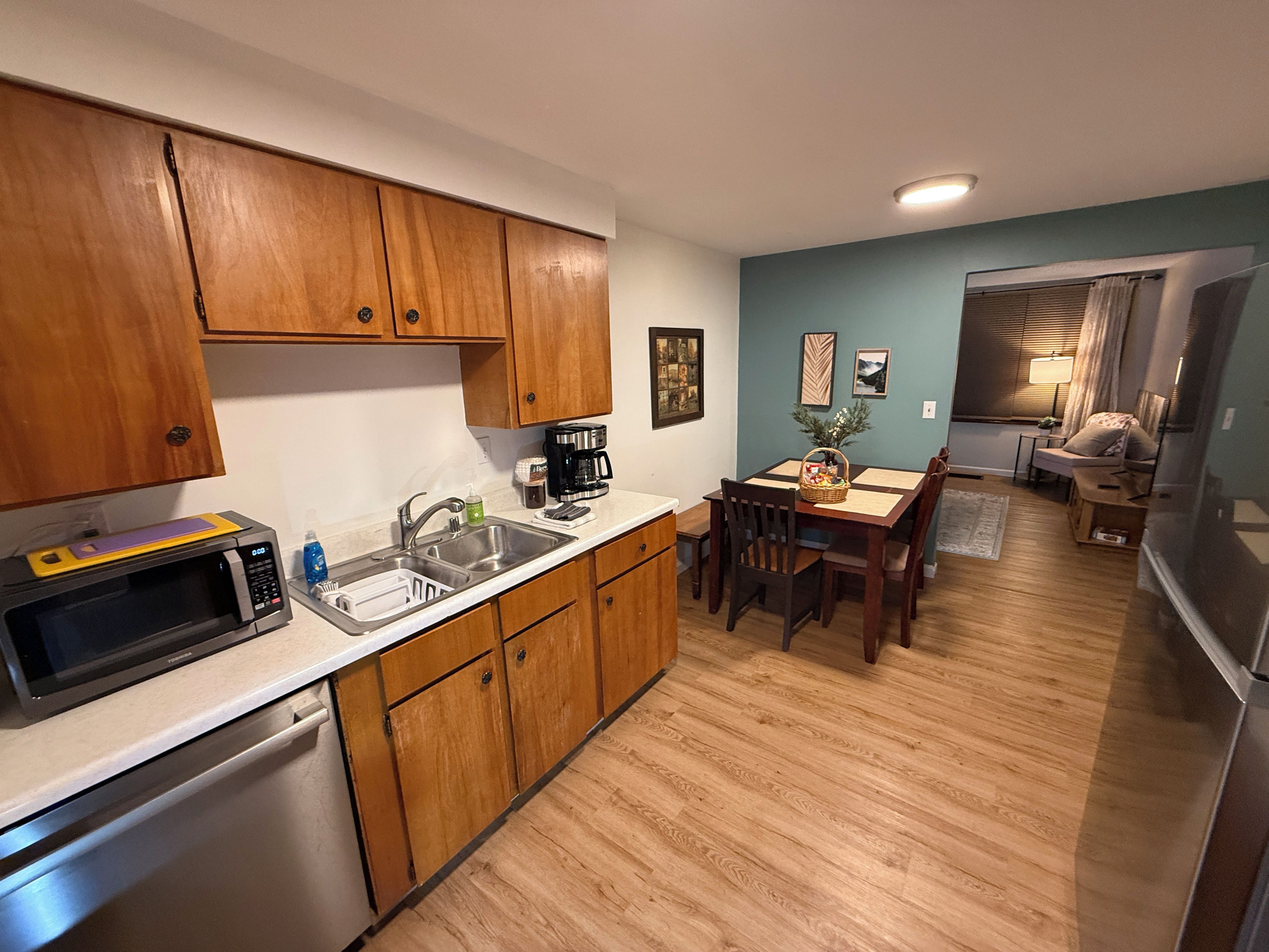 A compact kitchen with wooden cabinets, a microwave, a sink, and a dining area with a table and chairs.