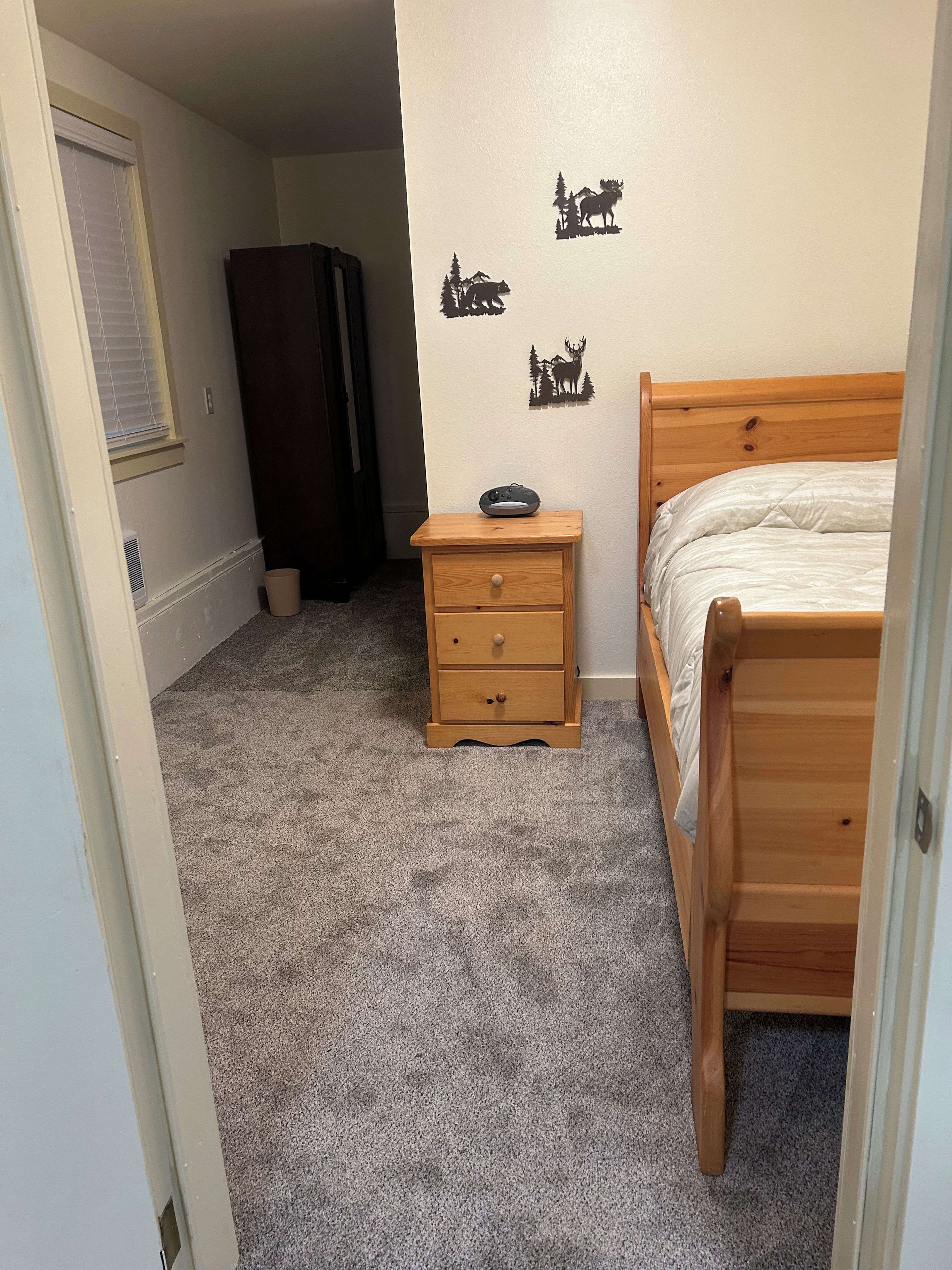 A bedroom with a wooden bed, a nightstand with a remote control, a dresser, and a wall decal of animals.